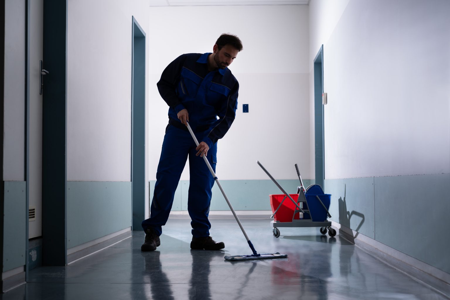 Man using a dust mop to clean a hallway